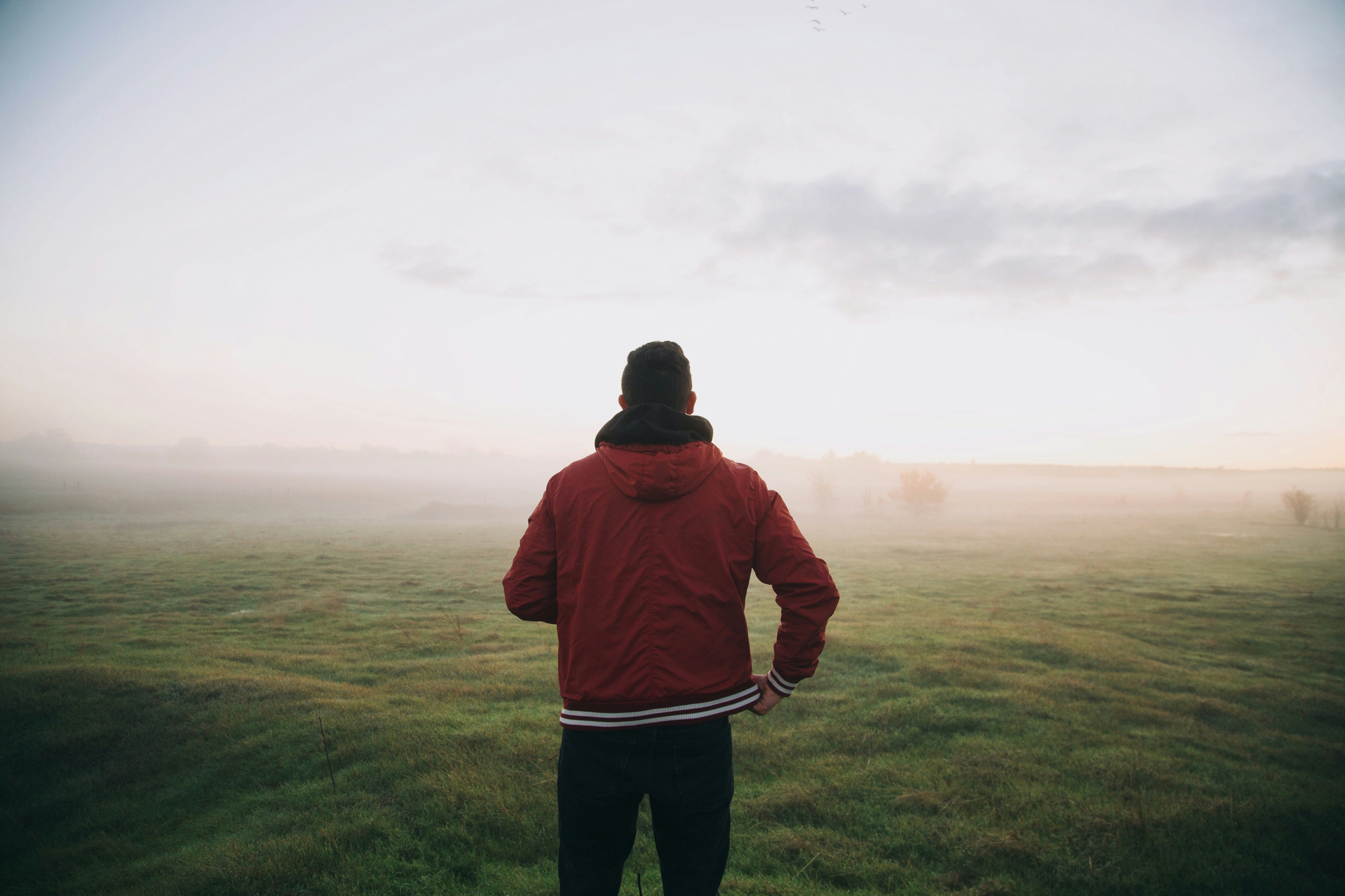 photo of man wearing red jacket facing horizon